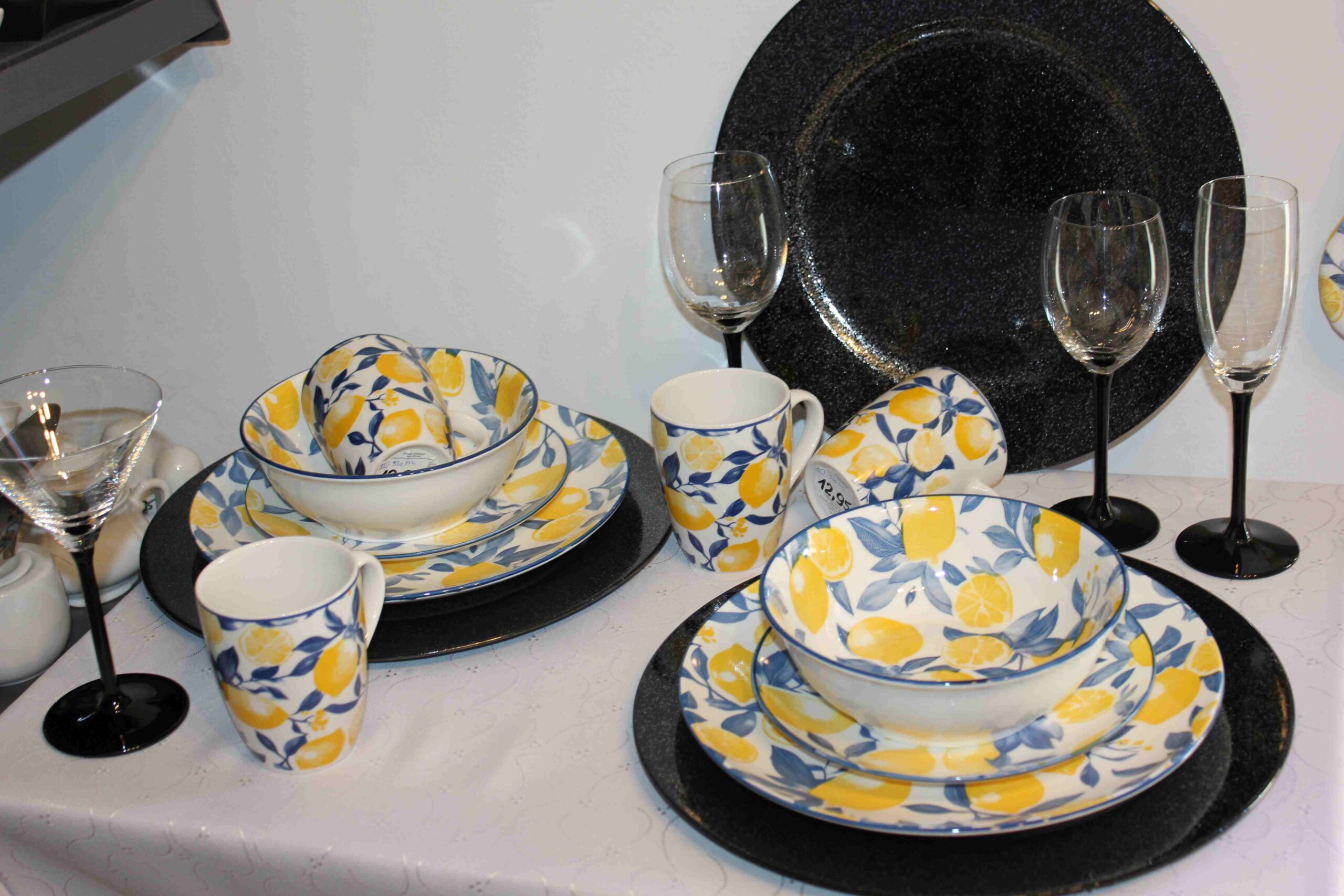 Porcelanowy serwis obiadowy w cytryny z niebieską obwódką, kubki, miski i talerze na czarnych podkładkach z kieliszkami